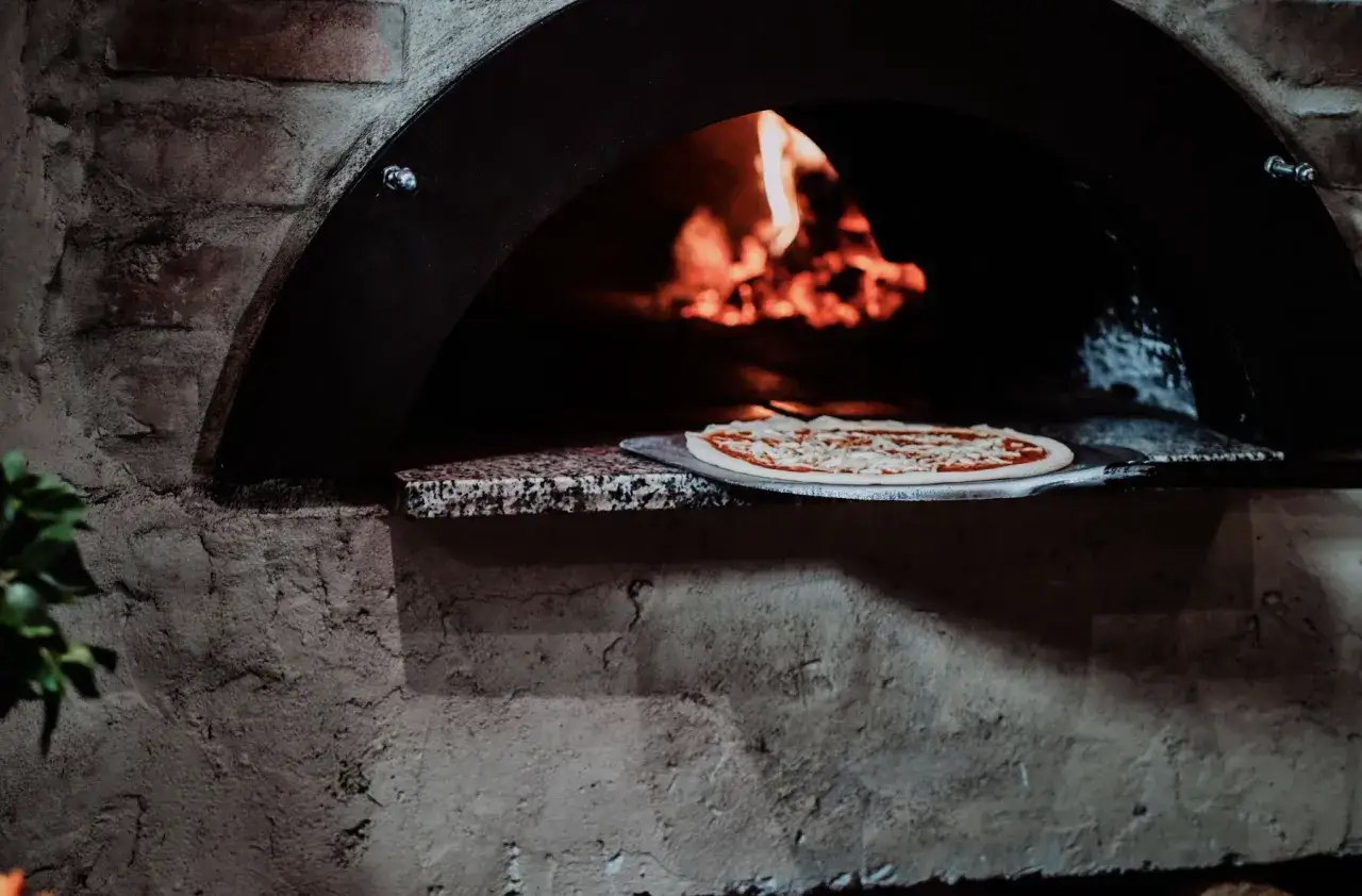 świeża pizza wkładana do dużego pieca ogrodowego
